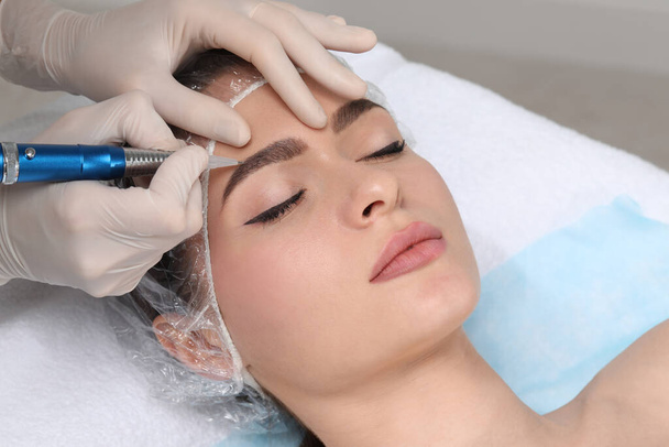 Young woman during procedure of permanent eyebrow makeup in beauty salon, closeup - Fotoğraf, Görsel