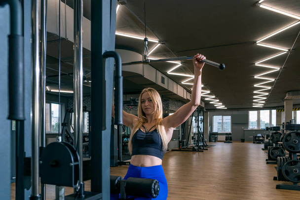 Attractive blond woman with beautiful figure is engaged in the empty gym. Upper block thrust. Healthy lifestyle. - Foto, imagen