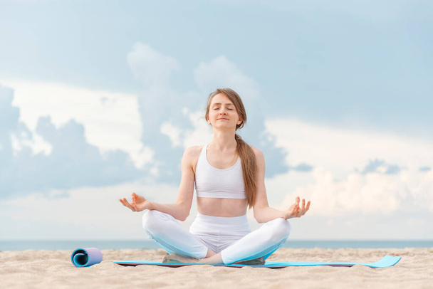 Yoga al amanecer en la playa. Joven hermosa mujer practicando yoga meditación al aire libre junto al mar. - Foto, imagen