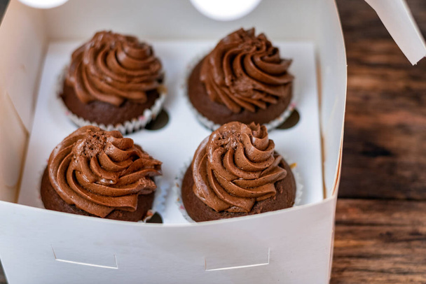 Set di quattro mafins al cioccolato in scatola di cartone. I cupcake sono decorati con crema al burro di cioccolato - Foto, immagini