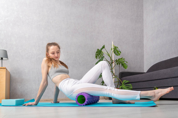 Jonge vrouw masseren beenspier met schuim massage roller. Apparatuur voor MFR. Roller voor fysiotherapie - Foto, afbeelding