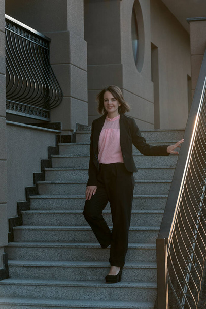 Successful elegant woman in formal business clothing outside. Woman wearing black suit. Young woman ot the stairs. - Photo, Image