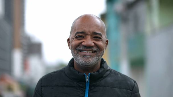 Счастливый пожилой черный мужчина с портретом, улыбающийся в камеру, стоящую снаружи на улице - Фото, изображение