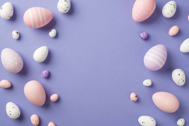 Vista superior de muchos huevos de Pascua multicolores de diferentes tamaños con rayas y puntos en el fondo aislado de color púrpura pastel con copyspace en el centro - Foto, imagen