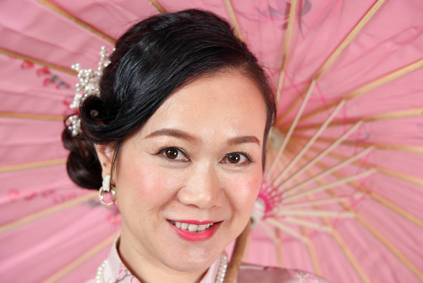 Çekici orta yaşlı kadın. Çinli Cheongsam elbisesi giyiyor. Renkli kağıt şemsiyeyle dans ediyor. - Fotoğraf, Görsel