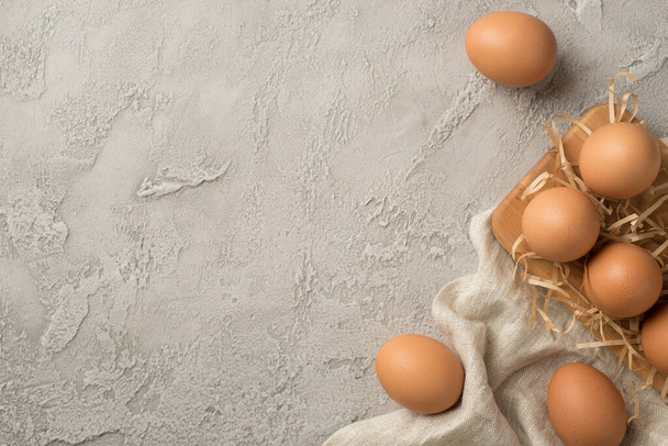 Top view photo of brown easter eggs cloth straw and wooden egg holder on isolated grey concrete background with copyspace - Φωτογραφία, εικόνα