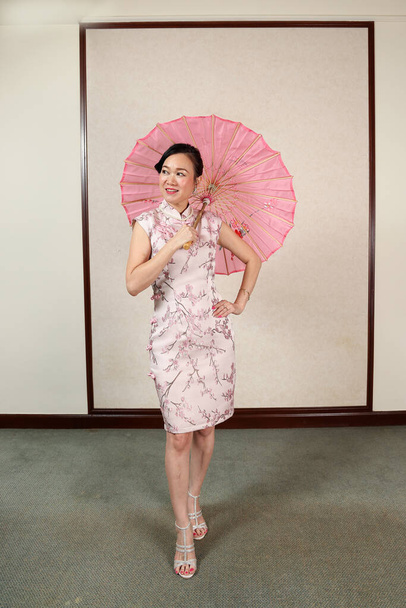 Attraktive Frau mittleren Alters in chinesischem Cheongsam-Kleid tanzt mit buntem Papierschirm posierend - Foto, Bild