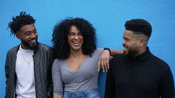 Three latin friends laughing and smiling leaning on blue wall spontaneous laughter - Foto, imagen