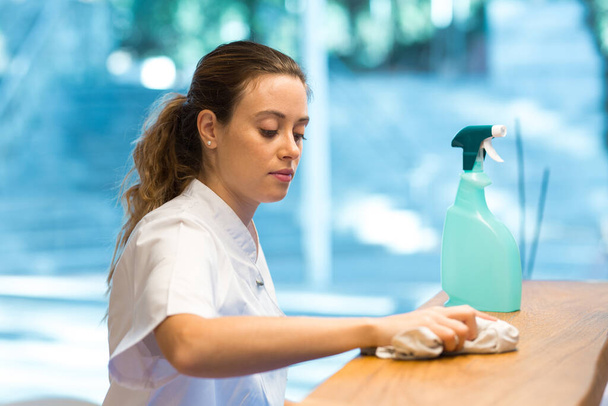 Mujer limpiando con contador desinfectante en clínica moderna - Foto, Imagen
