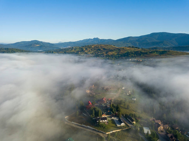 Mountain settlement in the Ukrainian Carpathians in the morning mist. Aerial drone view. - Фото, изображение