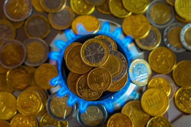 Σόμπα γκαζιού αναμμένη, με στοίβες νομισμάτων από πάνω της. Αύξηση του κόστους και των τιμολογίων φυσικού αερίου. - Φωτογραφία, εικόνα