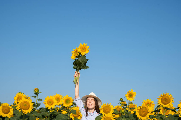 Happy woman hand raised above his head a bouquet of sunflowers on a background of blue sky. The concept of victory in Ukraine. High quality photo - Foto, immagini