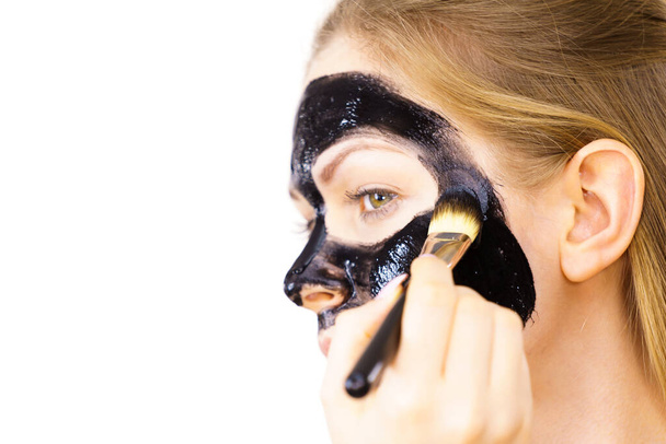 Молода жінка наносить пензлем чорну детоксикаційну грязьову маску на обличчя. Дівчина піклується про шкіру. Лікування краси. Догляд за шкірою
. - Фото, зображення