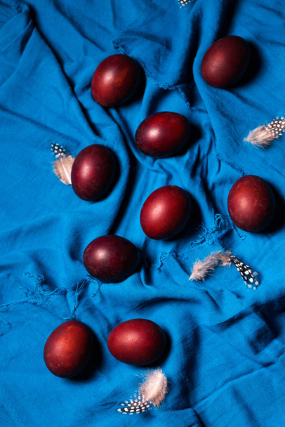 Красиві бордові яйця з пір'ям на синій тканині. Великодня концепція в сільському стилі
 - Фото, зображення