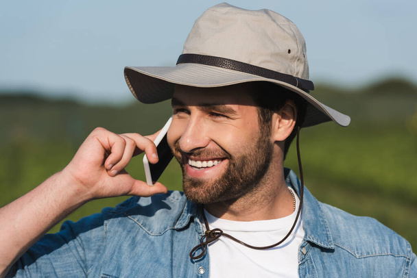joyful farmer in brim hat talking on mobile phone and looking away outdoors - Foto, imagen