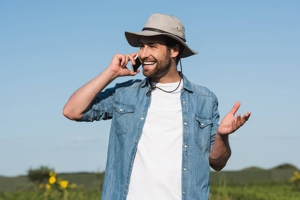 vidám farmer karimás kalapban mobilon beszél a szabadban - Fotó, kép