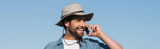 Gülümseyen çiftçi, mavi gökyüzüne karşı cep telefonuyla konuşurken yüzünü çeviriyor. - Fotoğraf, Görsel