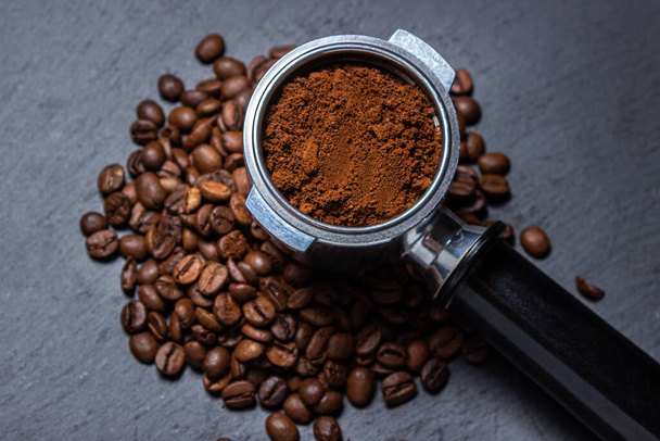 Café moulu et grains de café sur fond noir. Préparation du café dans une machine à café. - Photo, image