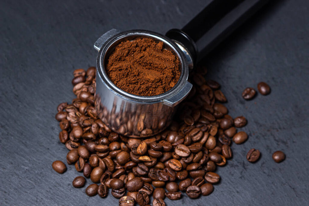 Ground coffee and coffee beans on a black background. Preparing coffee in a coffee machine. - Photo, image