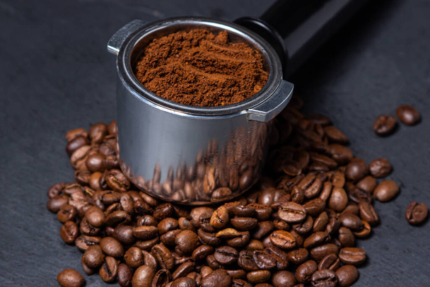 Gemalen koffie en koffiebonen op een zwarte achtergrond. Koffie bereiden in een koffiezetapparaat. - Foto, afbeelding