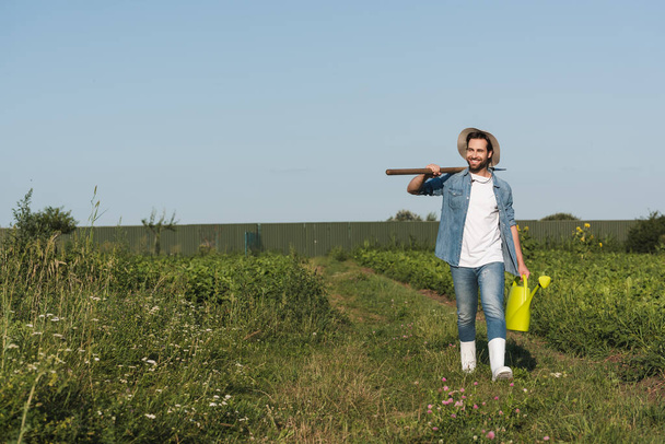 full length view of positive farmer with shovel and watering can walking in field - 写真・画像