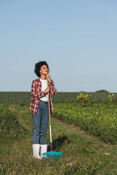 full length view of african american woman with rakes looking away in field - Foto, Imagem