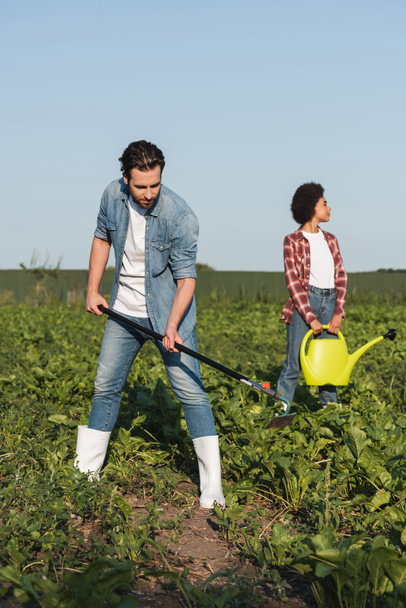 full length view of farmer working with hoe near african american woman with watering can - Photo, Image