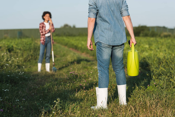 contadino in piedi con irrigazione può vicino offuscata donna africana americana  - Foto, immagini