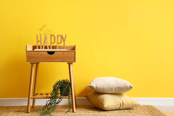Houten nachtkastje met decor nabij gele muur - Foto, afbeelding