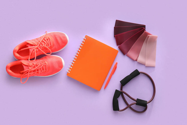 Gummibänder, Notizbuch, Stift, Fitness-Expander und Schuhe auf farbigem Hintergrund - Foto, Bild