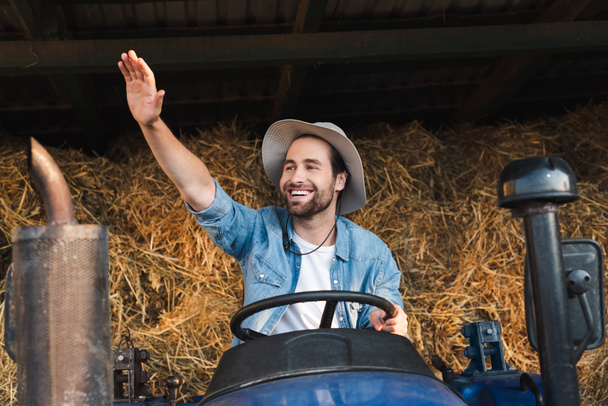 Fröhlicher Bauer auf Traktor schaut weg und winkt - Foto, Bild