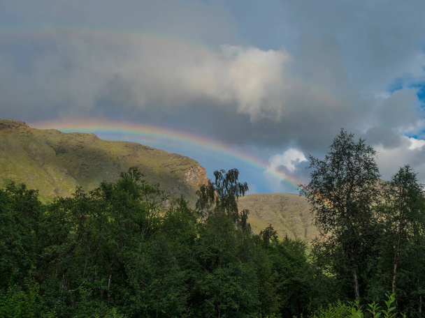 Regenbogen über grüne Hügel, Berge und Birkenwälder in der schwedischen Landschaft Lapplands am Padjelantaleden-Wanderweg. Sommerlicher bewölkter Tag - Foto, Bild