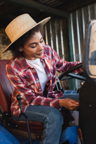 young african american woman in straw hat starting tractor on farm - Foto, Bild