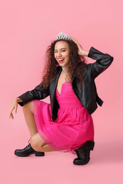 Beautiful young African-American woman in stylish dress, leather jacket and tiara on pink background - Photo, Image