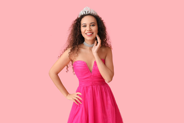 Hermosa mujer afroamericana joven en vestido elegante y tiara sobre fondo rosa - Foto, Imagen