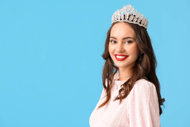 Beautiful young woman in stylish dress and tiara on blue background - Photo, Image