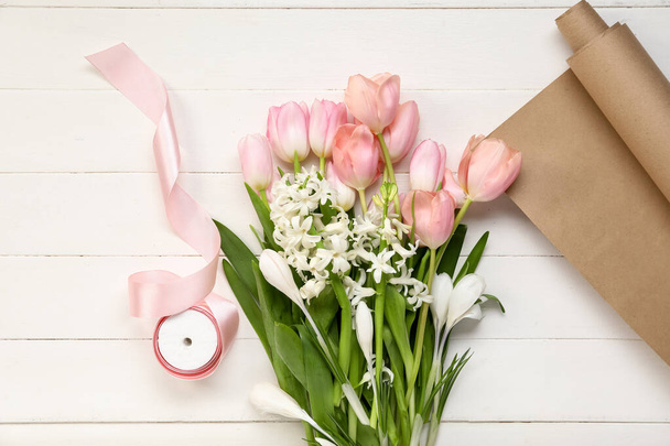 Csokor gyönyörű tavaszi virágok, szalag és csomagolópapír könnyű fa háttér - Fotó, kép