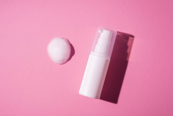 Botella blanca de plástico con bomba y la apariencia de la textura de la espuma sobre un fondo rosa. Cuidado de la piel cosmética de limpieza en la vista superior. Concepto de belleza para el cuidado corporal facial - Foto, imagen