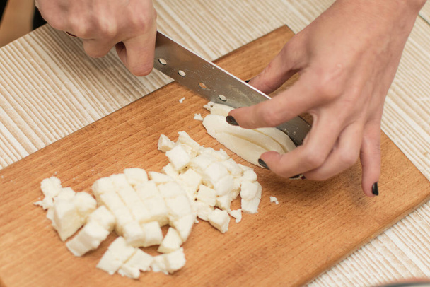 Woman slices cheese on a cutting board. - Фото, изображение