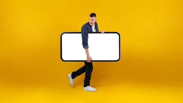 Guy Carrying Big Phone With Blank Screen Over Yellow Background - Photo, Image