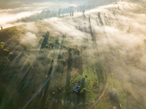 O nevoeiro envolve a floresta montanhosa. Os raios do sol nascente rompem o nevoeiro. Vista aérea de drones. - Foto, Imagem