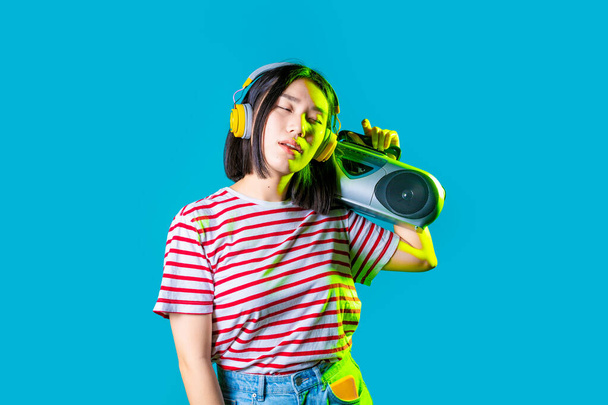 Young asiatic woman isolated listening music holding boombox listening music wireless headphones - Photo, Image