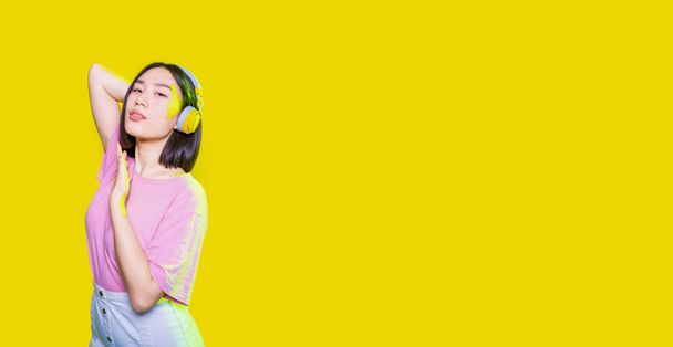 Young asiatic woman listening music headphones dancing isolated with confidence and attitude - cropped copyspace banner - Foto, immagini