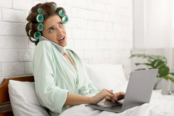 Verwirrte Hausfrau telefoniert mit Laptop im Schlafzimmer - Foto, Bild
