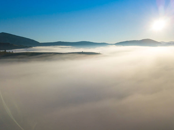 Flight over fog in Ukrainian Carpathians in summer. Mountains on the horizon. A thick layer of fog covers the mountains with a continuous carpet. Aerial drone view. - Photo, Image