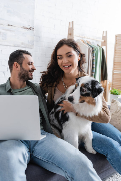 happy young couple watching movie on laptop near australian shepherd dog - Photo, Image