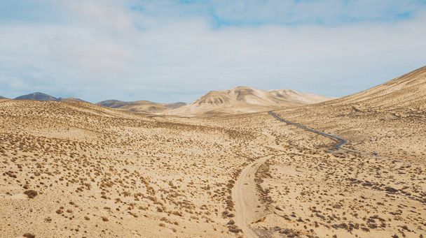 Path road in the middle of a mountains sand desert with blue bright sky in background. Concept of desertification or climate change for global warming. Amazing scenic travel destination - Photo, Image