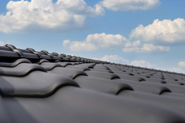 Ridge tegel op het dak van een eengezinswoning bedekt met een nieuwe keramische tegel in antraciet tegen de blauwe lucht. - Foto, afbeelding