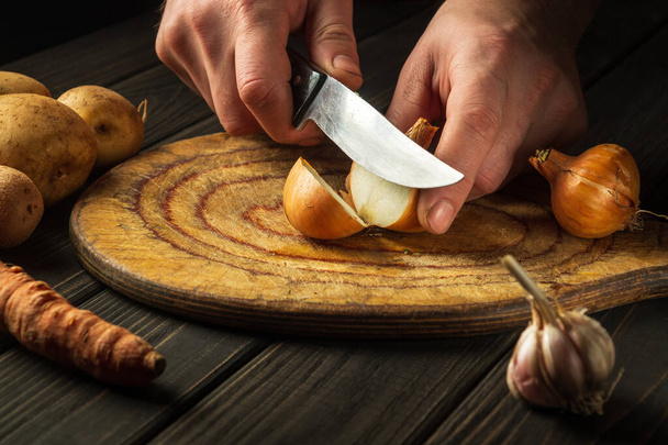 調理人の手でナイフでまな板の上に玉ねぎをスライス.ランチシェフの準備中のキッチンでの作業環境. - 写真・画像