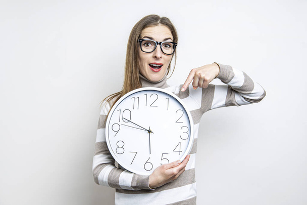 Surprised young woman pointing at wall clock on light background  - Photo, Image